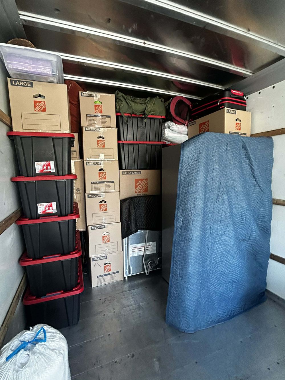Totes and labeled moving boxes stacked floor to ceiling beside a blanket-wrapped mattress in a Tulsa moving truck